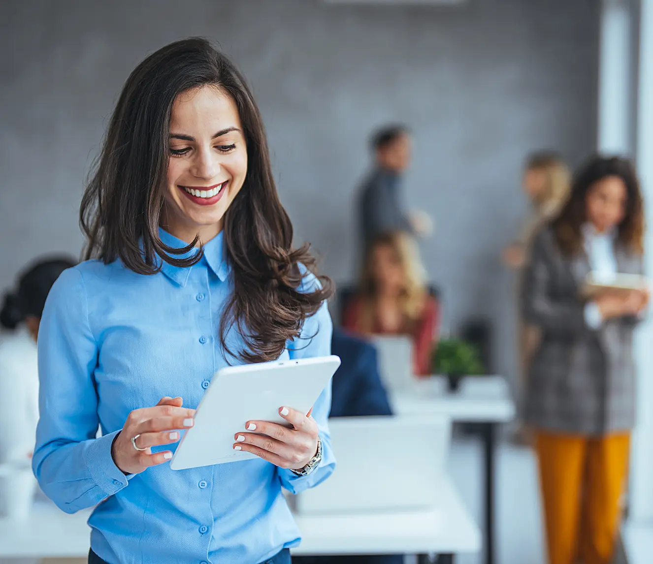white woman in blue shirt looking at tablet in bust office